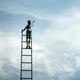 Figuur op hoge ladder reikt naar de wolkenlucht, symbolische weergave van ambitie en het najagen van dromen