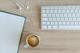 Minimalistisch bureau met wit toetsenbord, notitieblok, kopje koffie en witte oordopjes op houten tafelblad