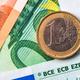 Een 1-euromunt ligt op eurobankbiljetten, met zichtbare ECB-markeringen die de authenticiteit van het geld aantonen.