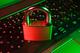 Rood hangslot op een verlicht gaming-toetsenbord met groene en rode verlichting, symboliseert cybersecurity