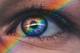 Close-up van een menselijk oog met een regenboog die eroverheen valt, wat resulteert in een kleurrijke iris met prismatische effecten.