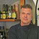 Een restaurantmedewerker in zwarte chef-jas staat voor een bar met flessen drank op de achtergrond