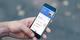 Hand houdt smartphone vast met mobiele app-interface voor financieel beheer of bankieren, met blauwe header en transactielijst.