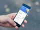 Hand houdt smartphone vast met mobiele app-interface voor financieel beheer of bankieren, met blauwe header en transactielijst.