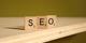 Houten Scrabble-letters vormen het woord "SEO" op een schuin oppervlak met groene achtergrond