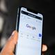 Hand houdt iPhone vast met Google-zoekpagina open op het scherm, closeup van het karakteristieke kleurrijke Google-logo