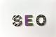 Het woord "SEO" gespeld met decoratieve letters in zwart-wit patronen en paars-groene print op witte achtergrond