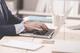 Persoon in zakelijke kleding werkt aan laptop op wit bureau met minimalistisch kantoormateriaal