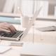 Persoon in zakelijke kleding werkt aan laptop op wit bureau met minimalistisch kantoormateriaal
