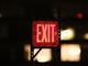 Verlicht rood exit-bord in een donkere ruimte met wazige lichtpunten op de achtergrond