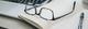 Leesbril op open notitieboek naast laptop en pen op wit bureau, moderne werkplek opstelling