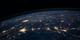 Nachtelijke luchtfoto van de aarde vanuit de ruimte, met lichtgevende steden en stedelijke gebieden die als gele lichtpunten oplichten.