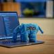 Laptop met programmeercode op scherm naast blauwe PHP-olifant mascotte, op houten bureau