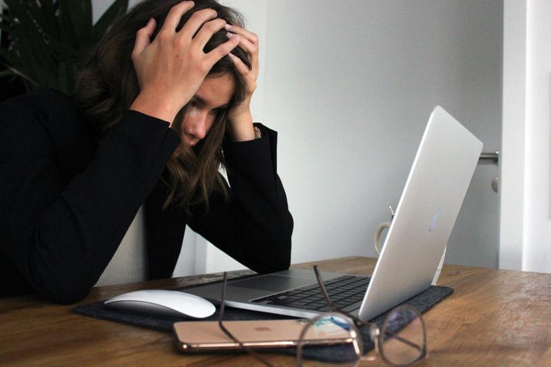 Persoon in zwarte kleding toont tekenen van stress en frustratie aan bureau met laptop en muis op houten tafel.