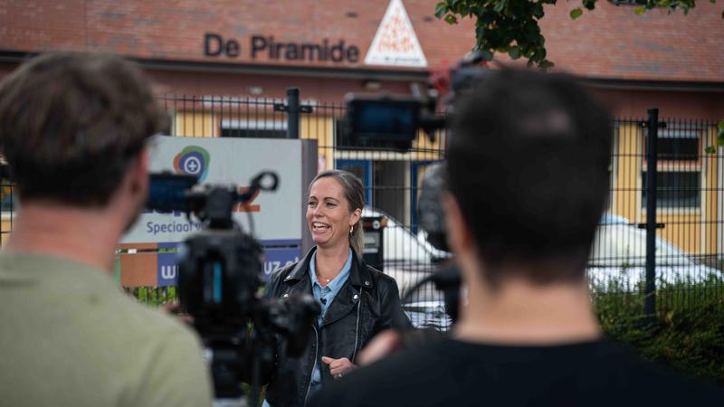 Vrouw buiten bij locatie gefilmd door twee cameramensen Vrouw wordt buiten geïnterviewd terwijl twee cameramensen haar filmen voor een videoproductie