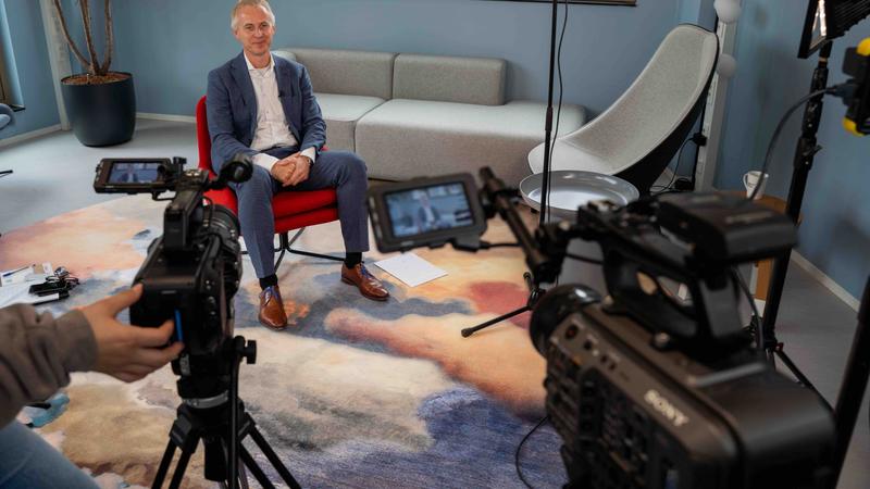 Man zittend in interview-opstelling, meerdere camera’s gericht op hem Man zit klaar voor een interview terwijl meerdere camera’s zijn opgesteld voor de opname