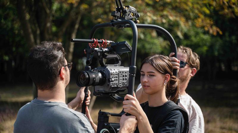Vrouw bedient camera in gimbal, team helpt, buitenlocatie Cameravrouw stelt een camera in op een stabilizer tijdens een video-opname in de buitenlucht