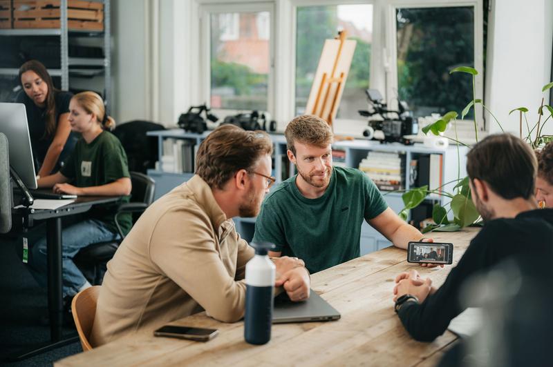 Team bespreekt een videoproductie aan tafel in een kantooromgeving Meerdere mensen aan tafel in kantoor, bespreken video op smartphone